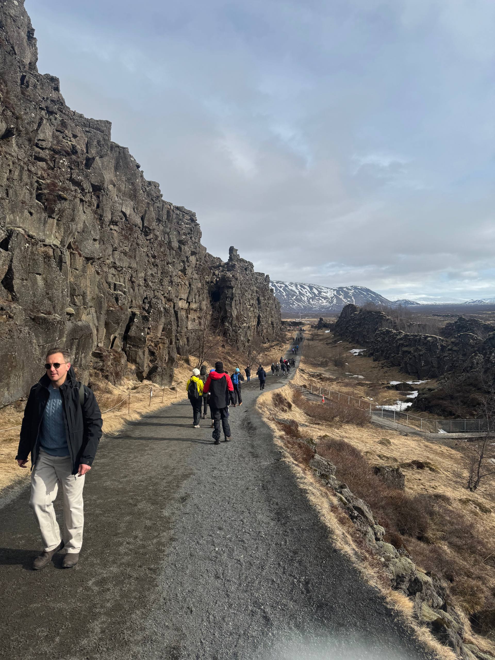 Visitors walking along the Almannagjá Gorge path between dramatic rock cliffs in Þingvellir National Park during a Day Trips From Reykjavik tour with our agency