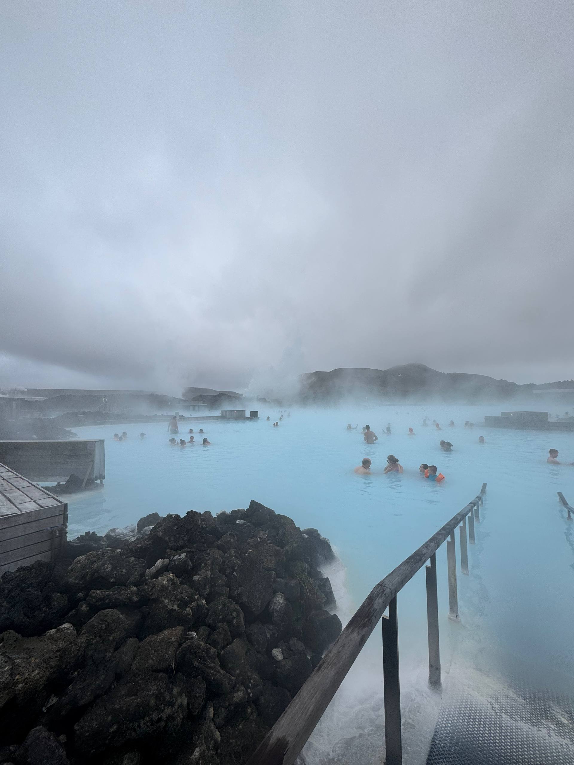 People enjoying the Blue Lagoon hot springs surrounded by Icelandic lava field during a Day Trips From Reykjavik guided tour with our agency