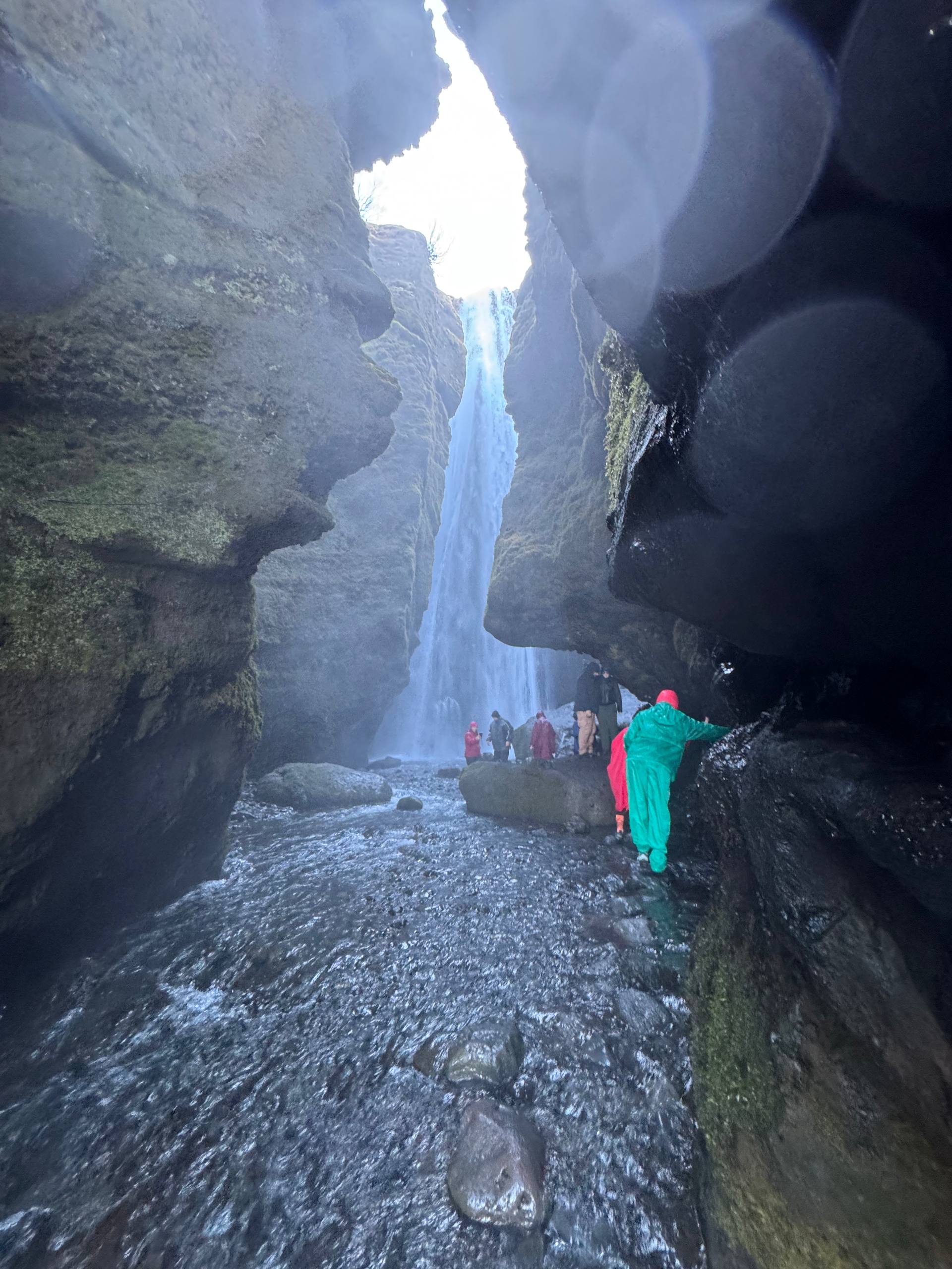 Gljúfrabúi waterfall tucked inside cliffs with tourists navigating wet rocks and water during a Day Trips From Reykjavik tour with our agency