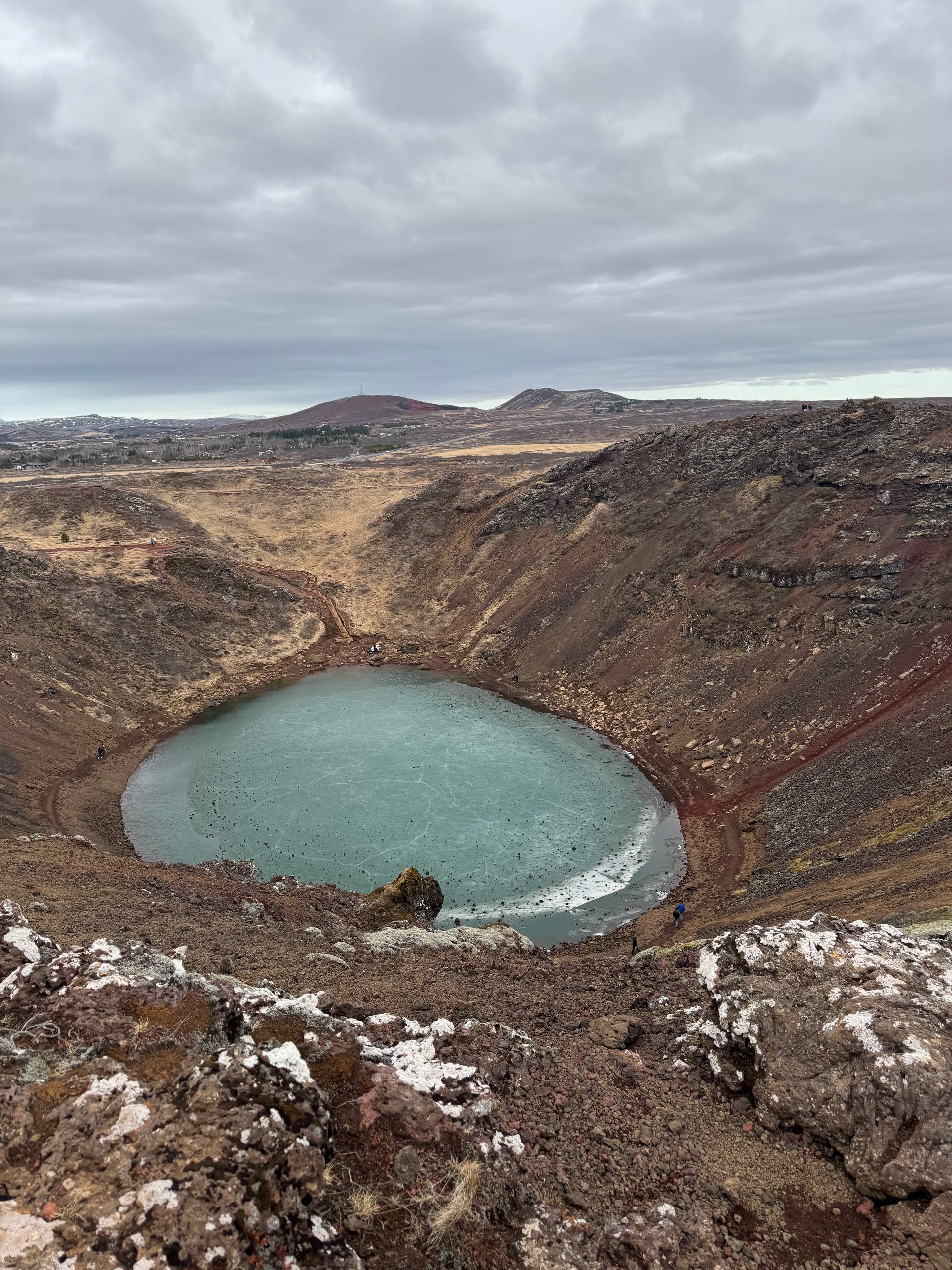 Kerið Crater volcanic lake with turquoise water surrounded by red rock slopes during a Day Trips From Reykjavik tour with our agency