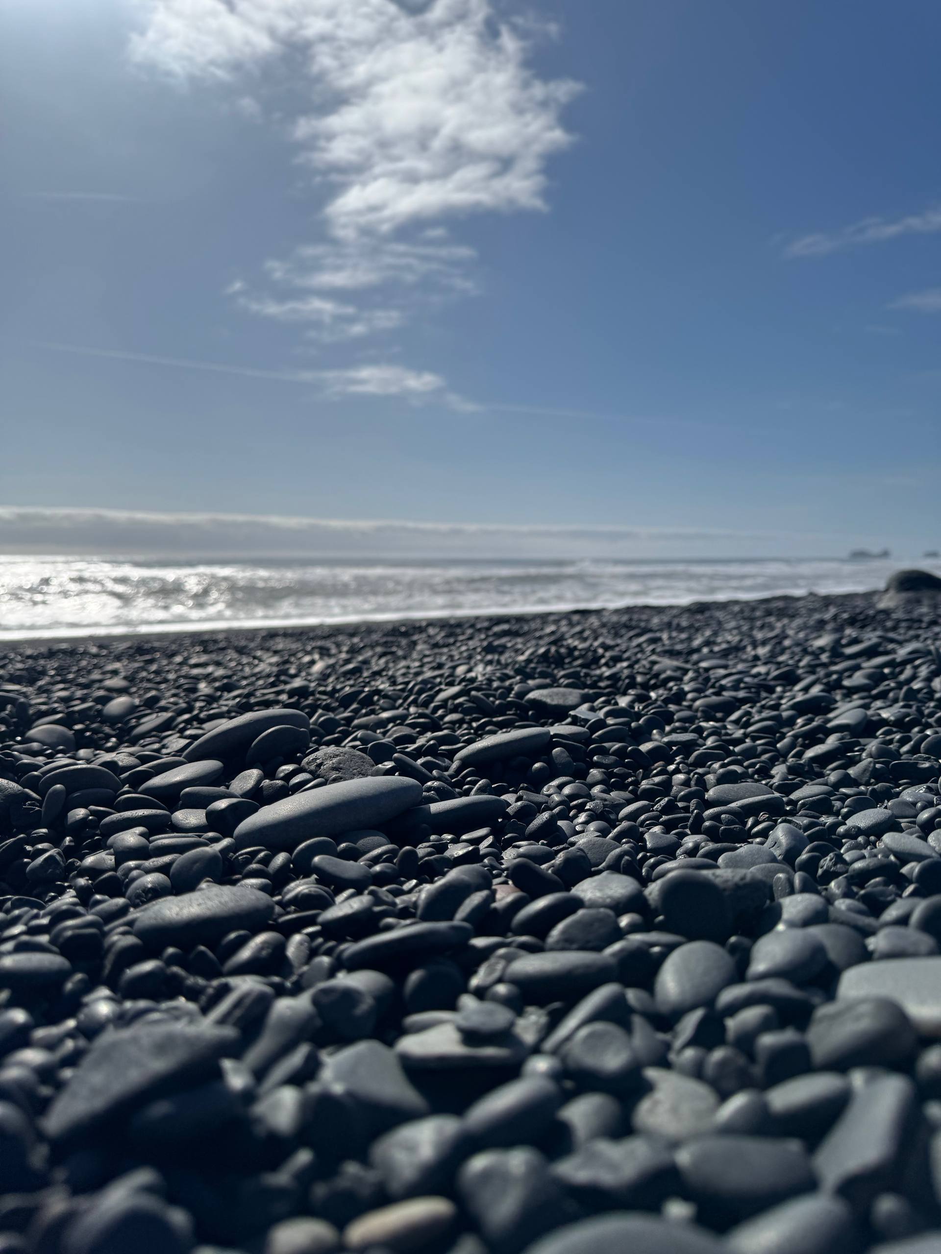 Reynisfjara Beach close-up showing smooth black pebbles and coastal scenery during a Day Trips From Reykjavik tour with our agency