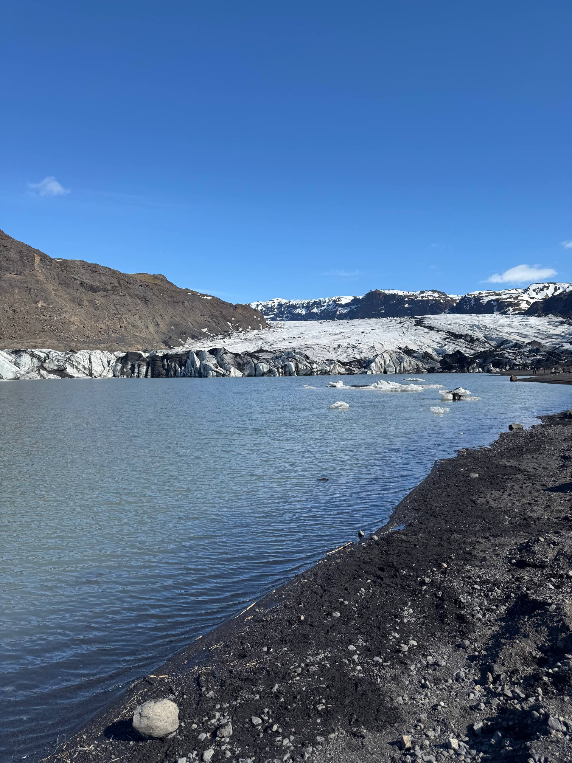 Sólheimajökull glacier lagoon in Iceland with floating ice and black volcanic shoreline during a Day Trips From Reykjavik tour with our agency