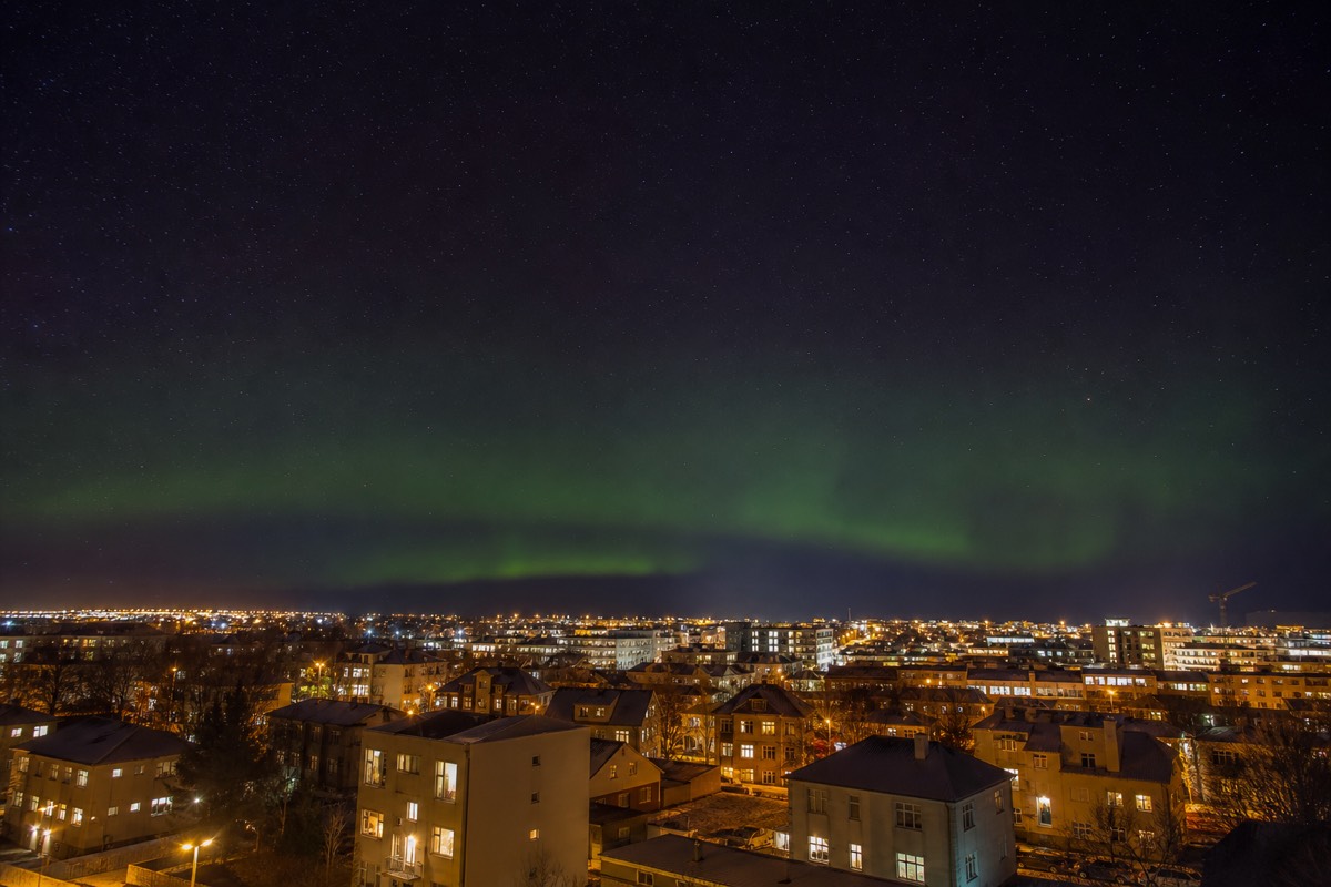 Green aurora over the coastline at the edge of Reykjavik with city lights below
