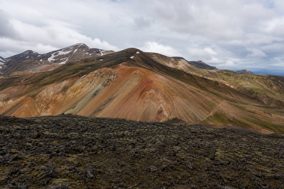 Banded rhyolite mountains in orange and green rising above the lava field at Landmannalaugar